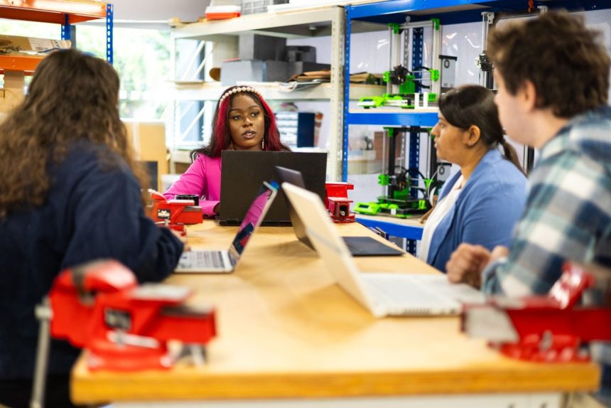 Grupo de estudantes participa de uma aula técnica colaborativa em um ambiente de oficina.