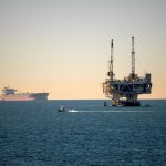 Plataforma de petróleo offshore acompanhada por um navio cargueiro em mar calmo durante o dia