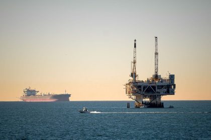 Plataforma de petróleo offshore acompanhada por um navio cargueiro em mar calmo durante o dia
