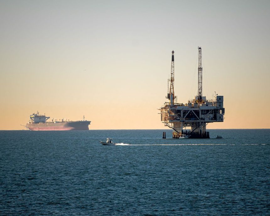 Plataforma de petróleo offshore acompanhada por um navio cargueiro em mar calmo durante o dia