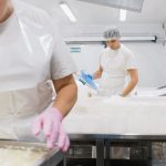 Trabalhadores usando equipamentos de proteção processam produtos em uma fábrica de alimentos.