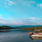 Barcos de pesca ancorados em uma margem tranquila, cercada por vegetação e montanhas.