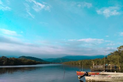 Barcos de pesca ancorados em uma margem tranquila, cercada por vegetação e montanhas.
