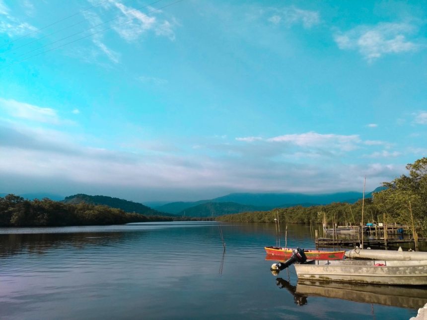 Barcos de pesca ancorados em uma margem tranquila, cercada por vegetação e montanhas.