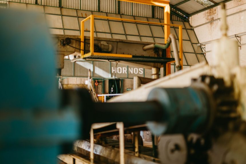 Detalhe de máquinas pesadas e esteiras transportadoras em operação no interior de uma fábrica.