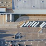 Vista aérea de um centro logístico com grandes galpões, caminhões e estacionamento.
