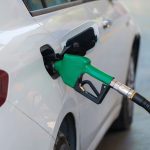 Bico verde abastece um carro branco em um posto de combustíveis.