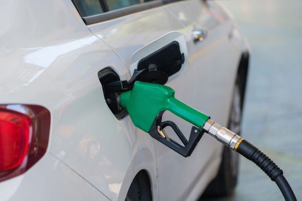 Bico verde abastece um carro branco em um posto de combustíveis.