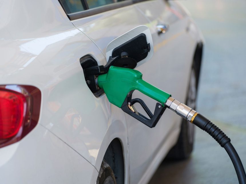 Bico verde abastece um carro branco em um posto de combustíveis.