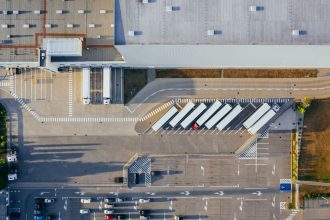 Vista aérea de um centro logístico com grandes galpões, caminhões e estacionamento.